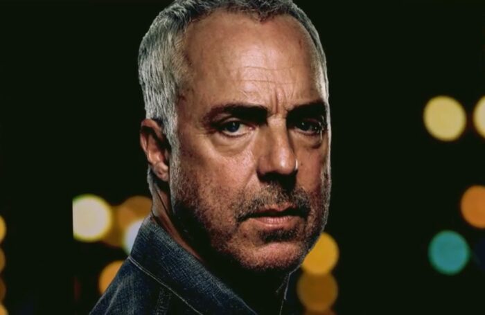 Titus Welliver stares off into the distance with glowing lights behind him 