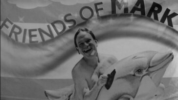 A young Mark McKinney clings to a dolphin with the words Friends of Mark written above him in The Kids in the Hall "Flags of Mark"