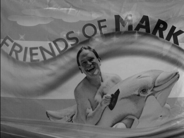 A young Mark McKinney clings to a dolphin with the words Friends of Mark written above him in The Kids in the Hall "Flags of Mark"