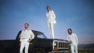 The Killers stand on and around a black pickup truck against a blue sky