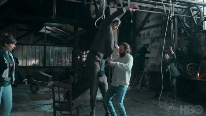 Image from Irma Vep: Edmond (Vincent Lacoste) dangles from a harness as Rene (Vinent Macaigne) attempts to assist.