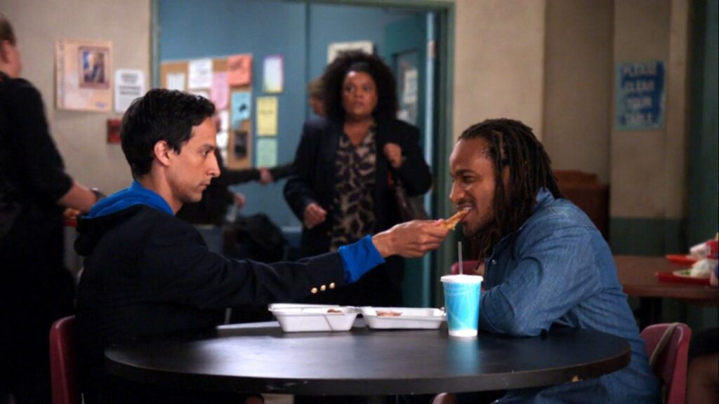 Abed feeding chicken fingers to Shirley's boyfriend, while she watches
