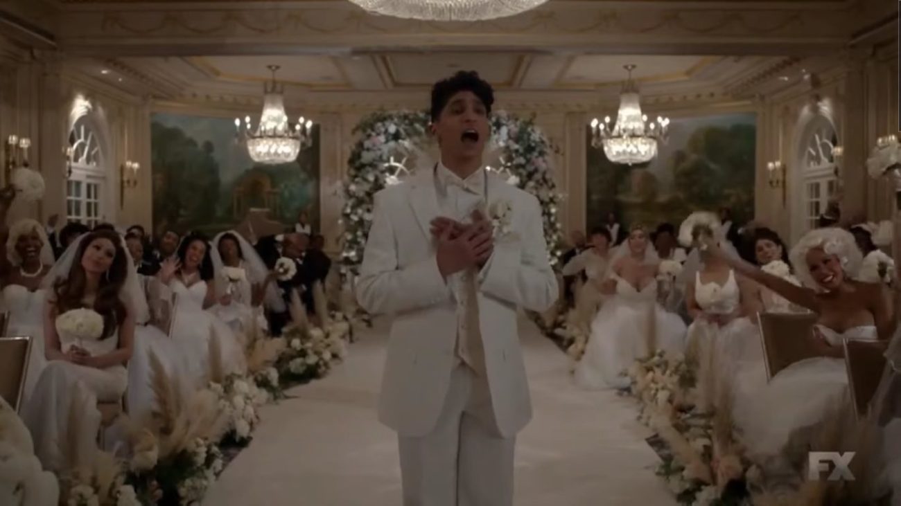 Papi sings from the aisle at his wedding, surrounded by guests wearing their own wedding dresses