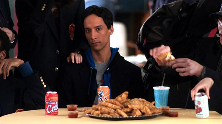 Abed (Danny Pudi) sitting at a table with a giant plate of chicken fingers and a hand on his shoulder