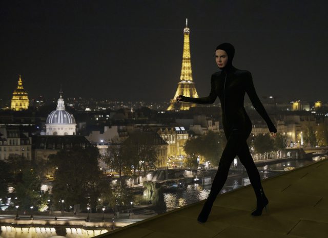 Mira in the catsuit with the Paris skyline behind her in Irma Vep
