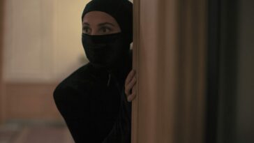 Image from Irma Vep: Alicia Vikander as Irma Vep in a catsuit, peering around a corner