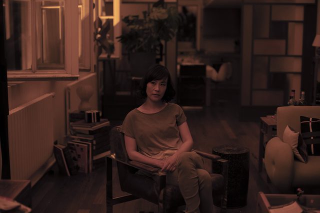 Image from Irma Vep: Jade Lee (Vivian Wu) sits and faces the camera in an apartment.