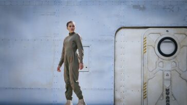 Bella stands on a walkway with a door to her side in the Moonhaven pilot
