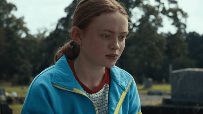 Max (Sadie Sink) in a blue jacket with trees in the background