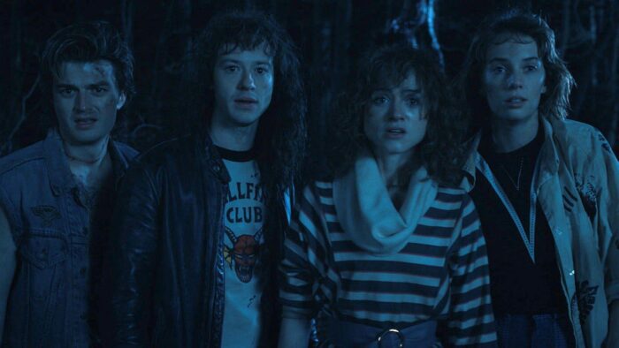 Steve, Eddie, Nancy, and Robin (the Stranger Things Season 4 dream team) stand looking forward awash in blue light