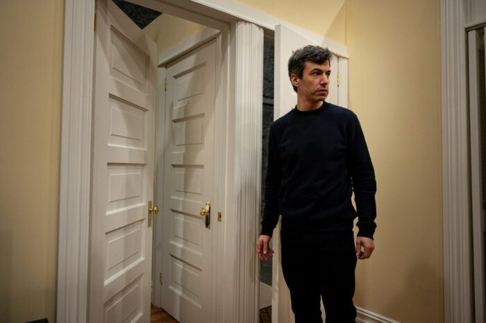 Nathan Fielder, dressed in black, stands near three doorways that are close together in The Rehearsal