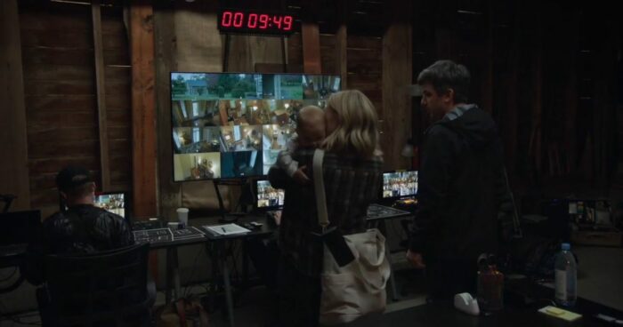 Nathan stands alongside a woman holding a baby, in front of a screen of video feeds in The Rehearsal S1E2, "Scion"
