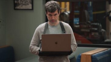 Nathan stands with an Apple laptop strapped around his shoulders such that it sits in front of his torso