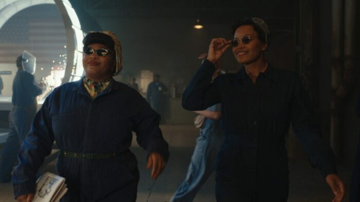 Gbemisola Ikumelo (Clance) and Chanté Adams (Max) walk in blue suits through a factory