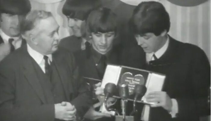 A hands-clasped Wilson watches as The Beatles inspect their Silver Heart awards.