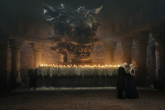 Viserys and Rhaenyra embrace in front of a dragon skull