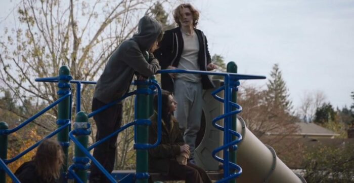 Joshua (who plays Adam) stands on the top of a playground slide, with other teens around him