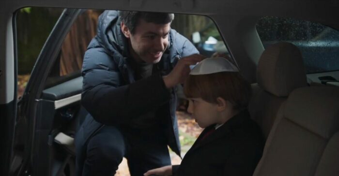 Nathan puts a Jewish head covering onto Adam's head