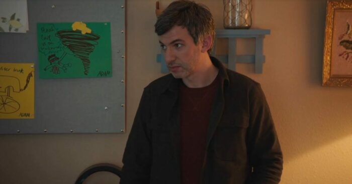 Nathan stands in front of a wall with drawings Adam made, including one where a guy is punching a volcano