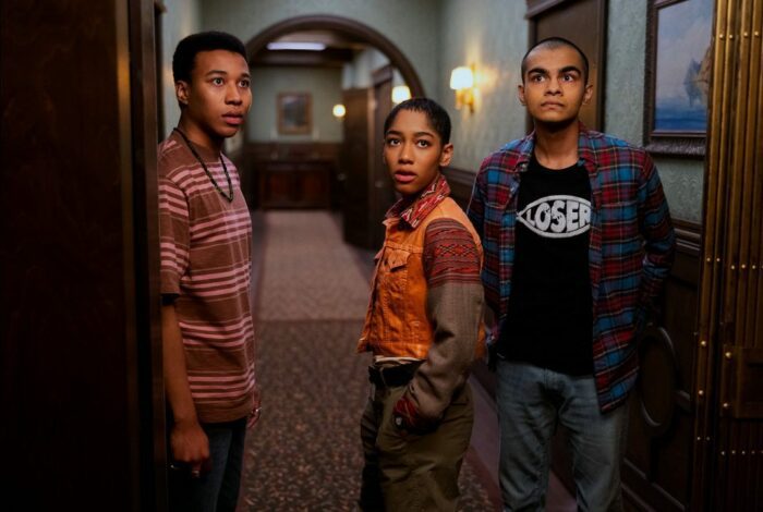 Three youths stand in a hallway looking concerned