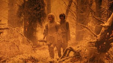 Galadriel and Theo walk through a forest covered in ash in an eerie orange light