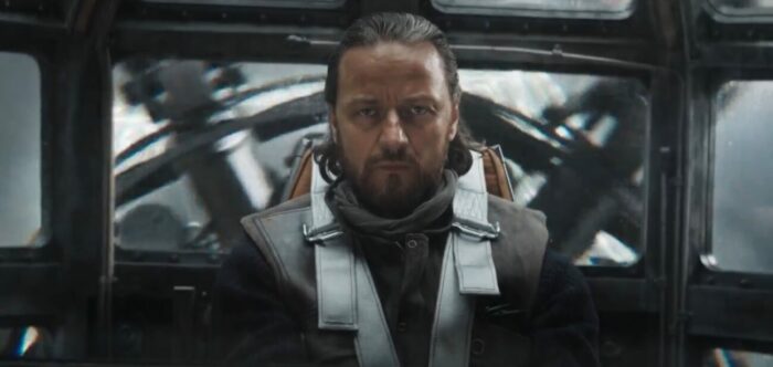 Lord Asriel sits strapped into a pilot's seat, with a stern look of concentration