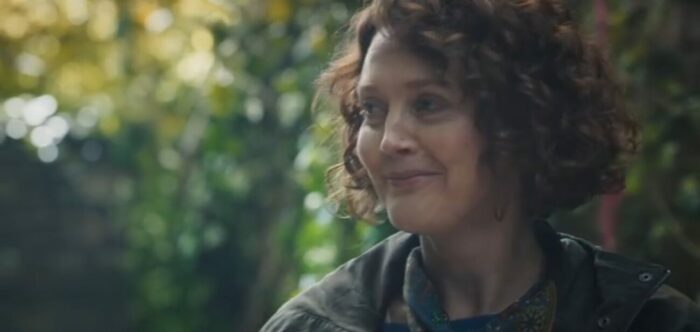 His Dark Materials S3E1-2 - Mary Malone sits in a garden with a knowing smirk on her face