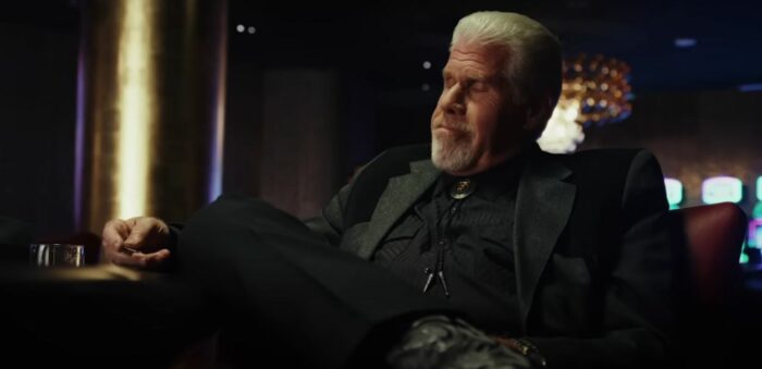 Ron Perlman reclining, dressed in black, in Poker Face