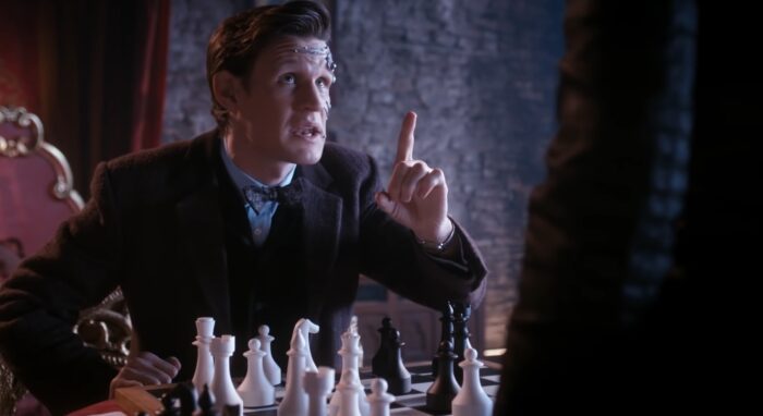 The Cyberplanner Doctor holds up a finger while sitting in front of a large chess set