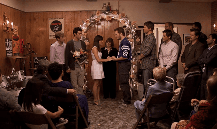 Andy and April getting married in their living room. Andy has six groomsmen including Tom, Chris, Ron and his bandmates. April's bridal party are Ben and Derek. 