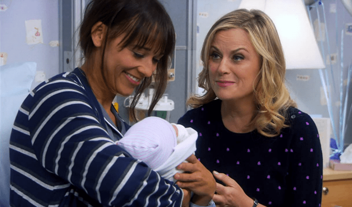Ann looks at baby she holding as Leslie looks at her lovingly, in a hospital room