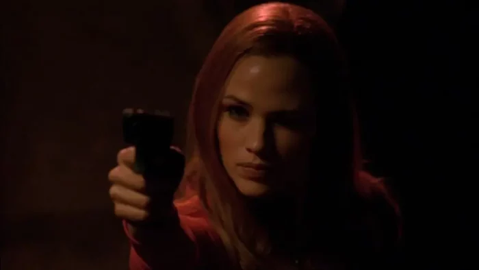Syd holds a gun, darkness behind her