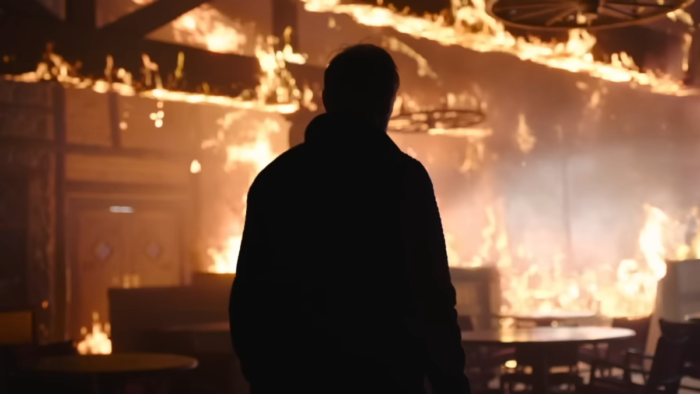 David (Scott Shepherd) from The Last of Us in eerie silhouette against a backdrop of fire.