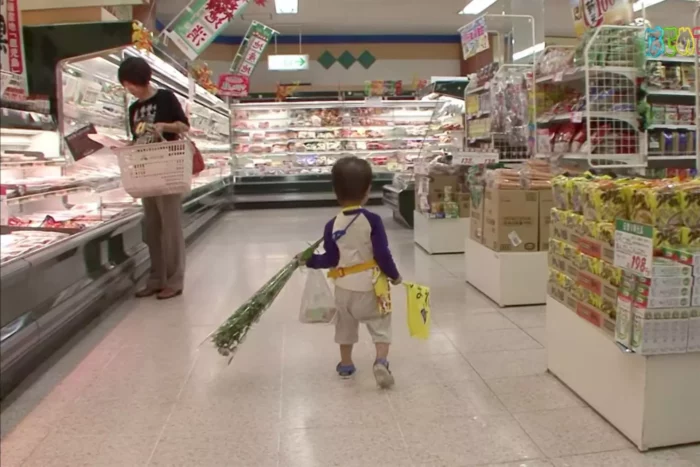 A still from Old Enough! where we're following a small boy, carrying several items, through a supermarket that seems expansive compared to his small size.