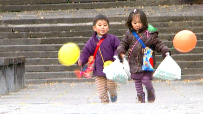 A boy and girl, siblings, are bundled up in winter coats and Japanese charm bags carry a bunch of things home, including plastic shopping bags and a helium balloon apiece.