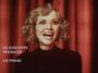 Misty smiling with an open mouth, wearing a black turtleneck, in front of a red curtain, in the Yellowjackets Season 2 opening credits