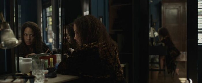 Tai sits in front of a mirror, with her reflection looking over at her, in Yellowjackets S2E2