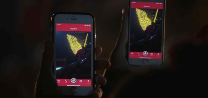 Mrs. Davis S1E3 - Two cells phones are held on screen with images of Wiley projected with glowing wings