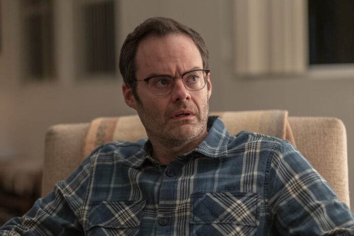 Barry as Clark, wearing glasses and looking up from a chair
