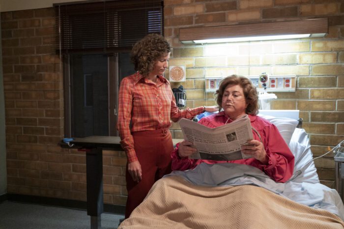 Dita Beard reads a newspaper in her hospital bed as her daughter stands beside her. 