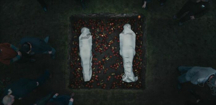 Two bodies wrapped in white, in a hole, surrounded by apples, in Silo S1E5 "The Janitor's Boy"