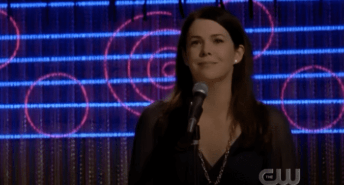 Lorelai stands in front of a microphone
