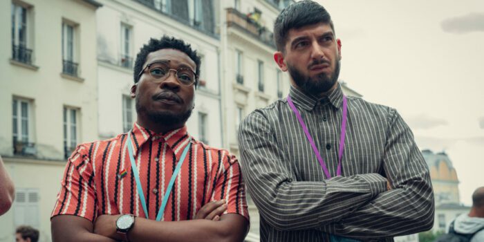 Fisayo Akinade as Mr Ajayi and Nima Taleghani as Mr Farouk standing next to each other in Paris. 