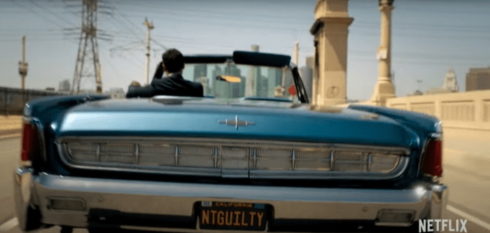 A man drives a blue convertible across a bridge, with the rear license plate saying NTGUILTY 