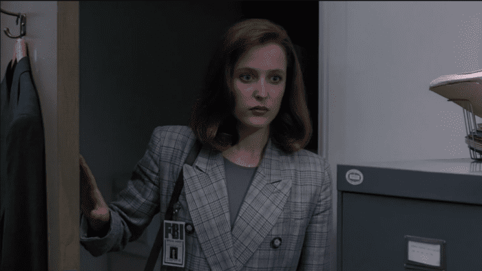 Scully (Gillian Anderson) enters Mulder's office for the first time, holding the door open