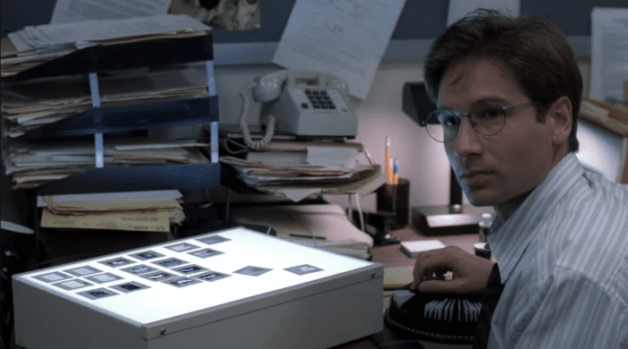 Mulder (David Duchovny) sits at his office desk studying photos