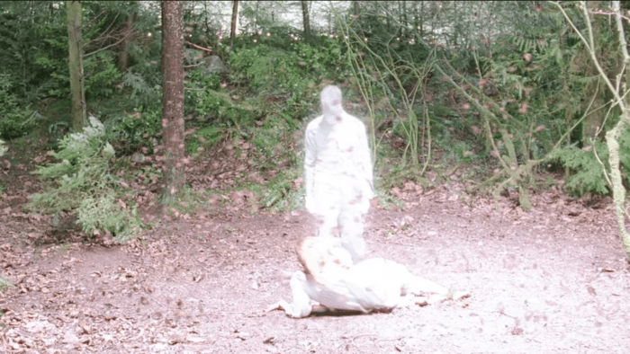 A young woman lies on the floor of a forest, with a strange figure looming over her, shrouded in white light