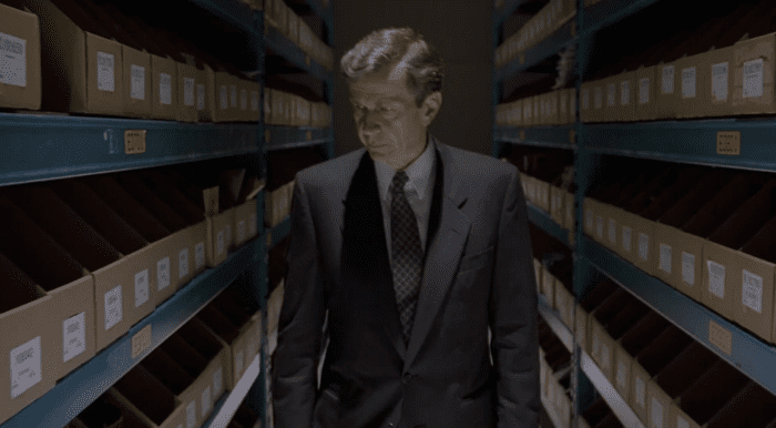 The Cigarette Smoking Man (William B. Davis) walking down a long corridor full of files