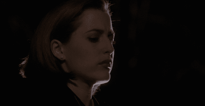 Agent Dana Scully, a woman with short red hair, stands in profile against a black background. Her face is faintly lit with white light.