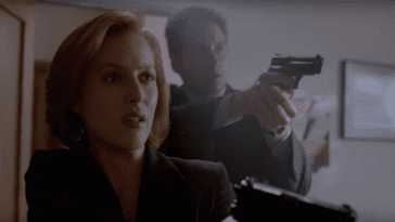Dana Scully (Gillian Anderson), a woman with short red hair wearing a dark blazer, holds up a pistol. Fox Mulder (David Duchovny) stands behind her; he wears a suit and also has a pistol raised.